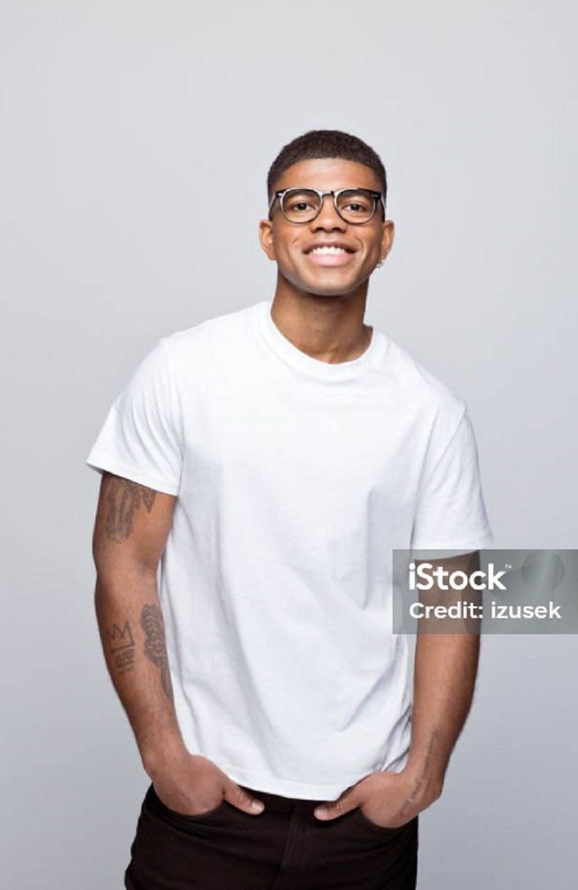 Happy african young man wearing white t-shirt and eyeglasses, standing with hands in pockets and smiling at camera. Studio portrait on grey background.